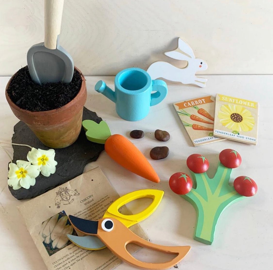 Set of colorful children's gardening toys including a pot, tools, and seed packets on a light surface.