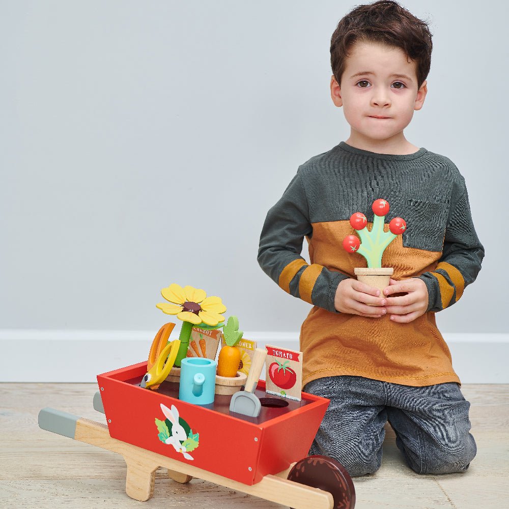 Child playing with a toy garden set on a light wooden floor.