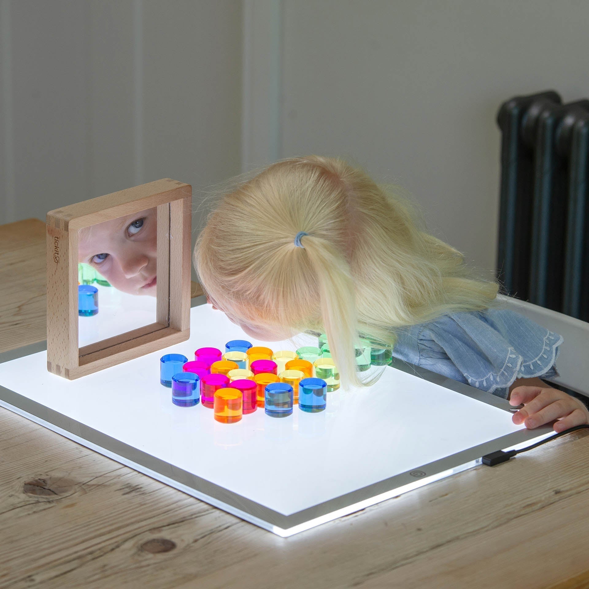 Child playing with colorful toys on a light-up table, with a mirror reflecting their face.