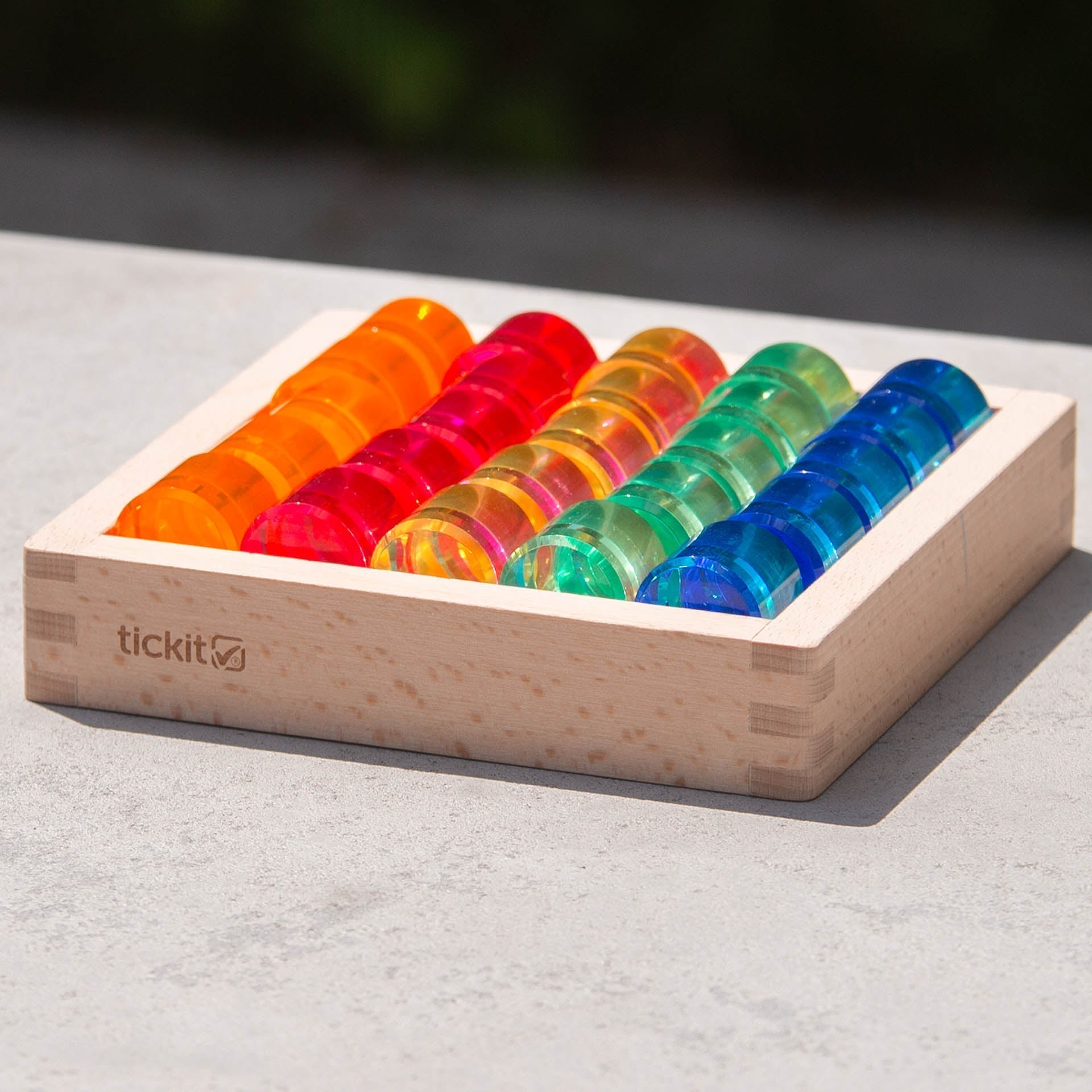 Colorful plastic tiles in a wooden tray on a light surface