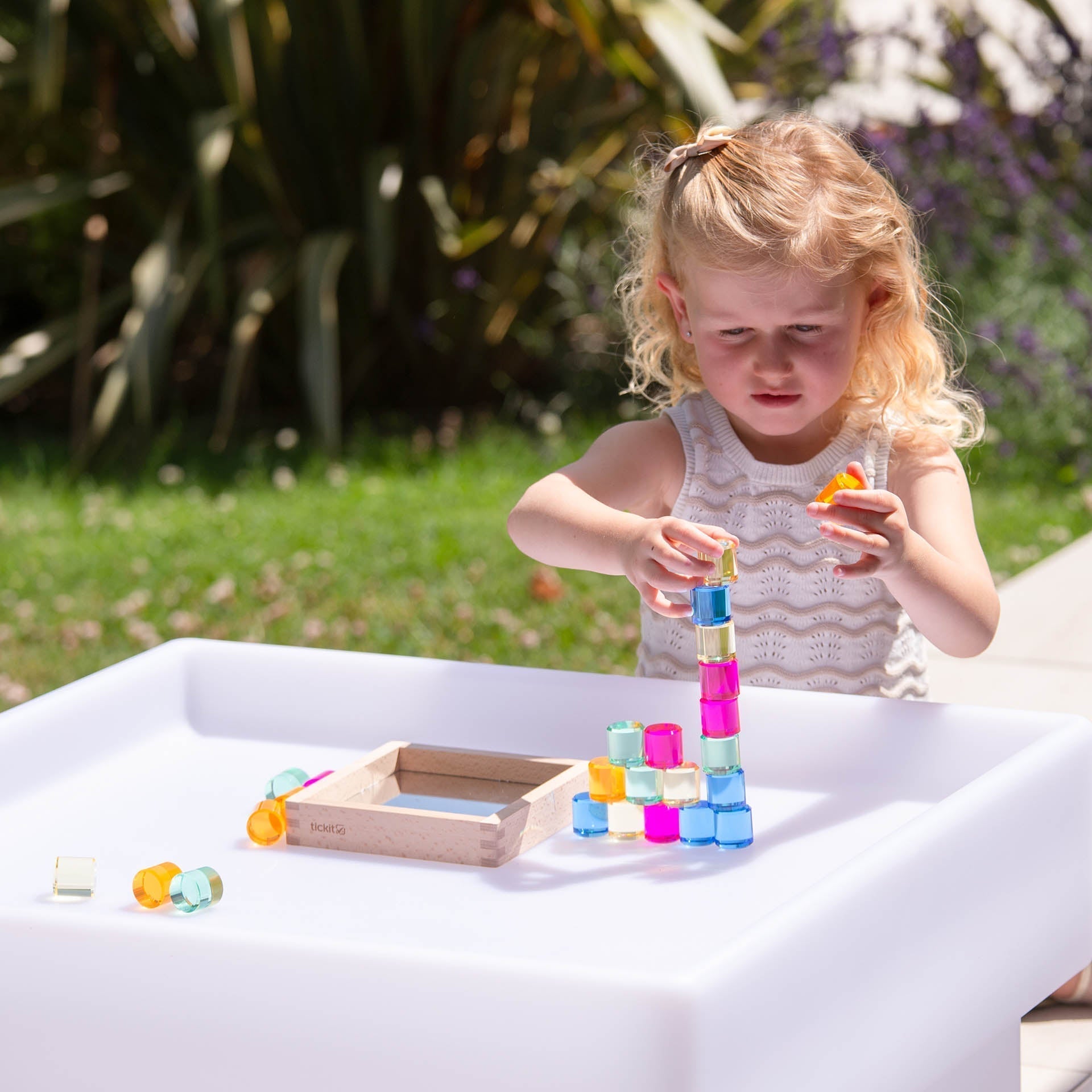 Child playing with colorful building blocks on a white table outdoors.