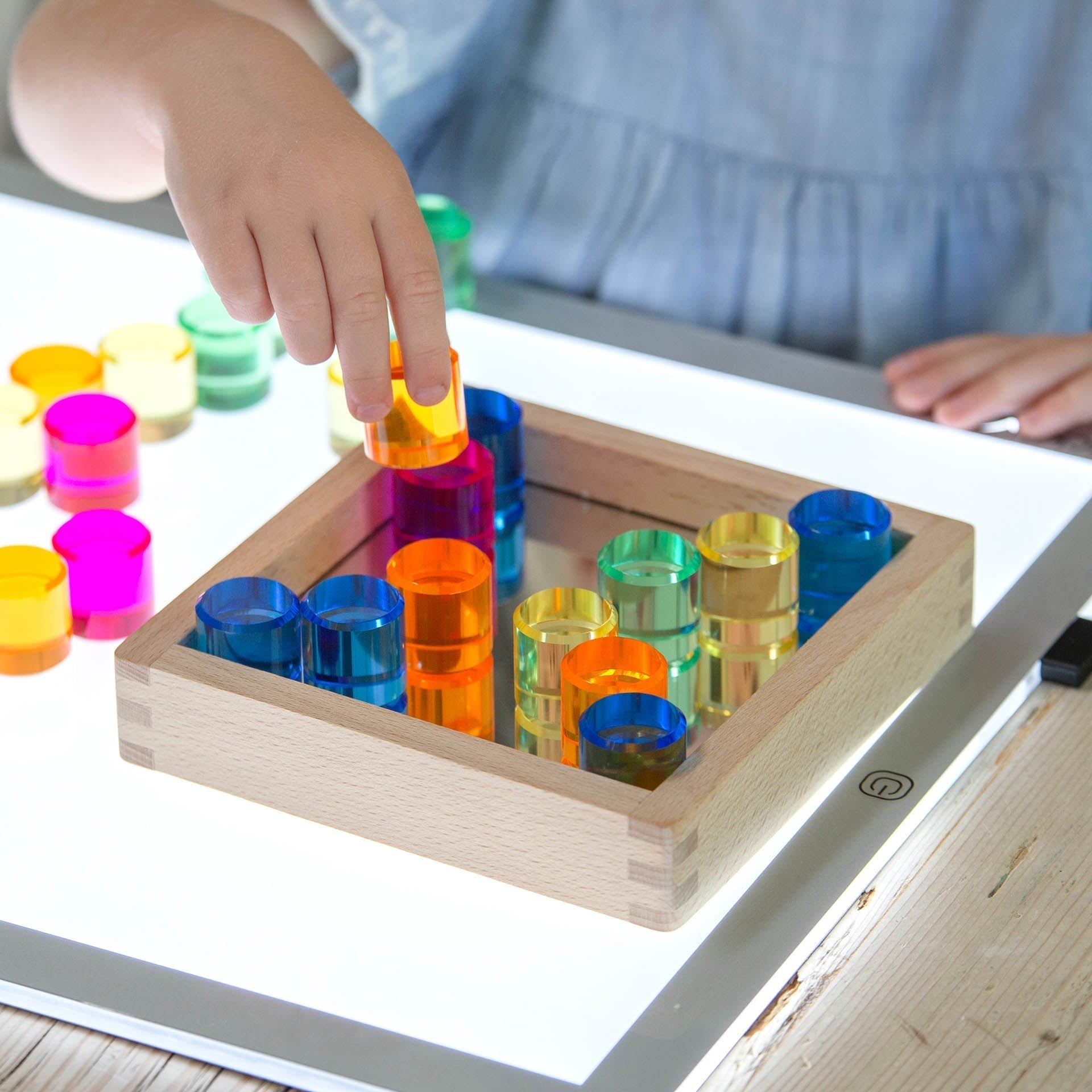 Child playing with a colorful transparent cups and boxes educational toy on a lightbox.