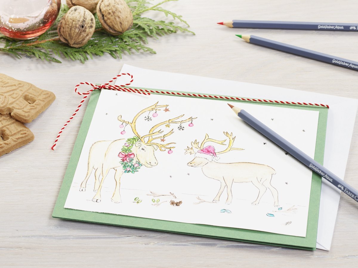 Christmas card with reindeer illustration on a table with cookies and pencils.