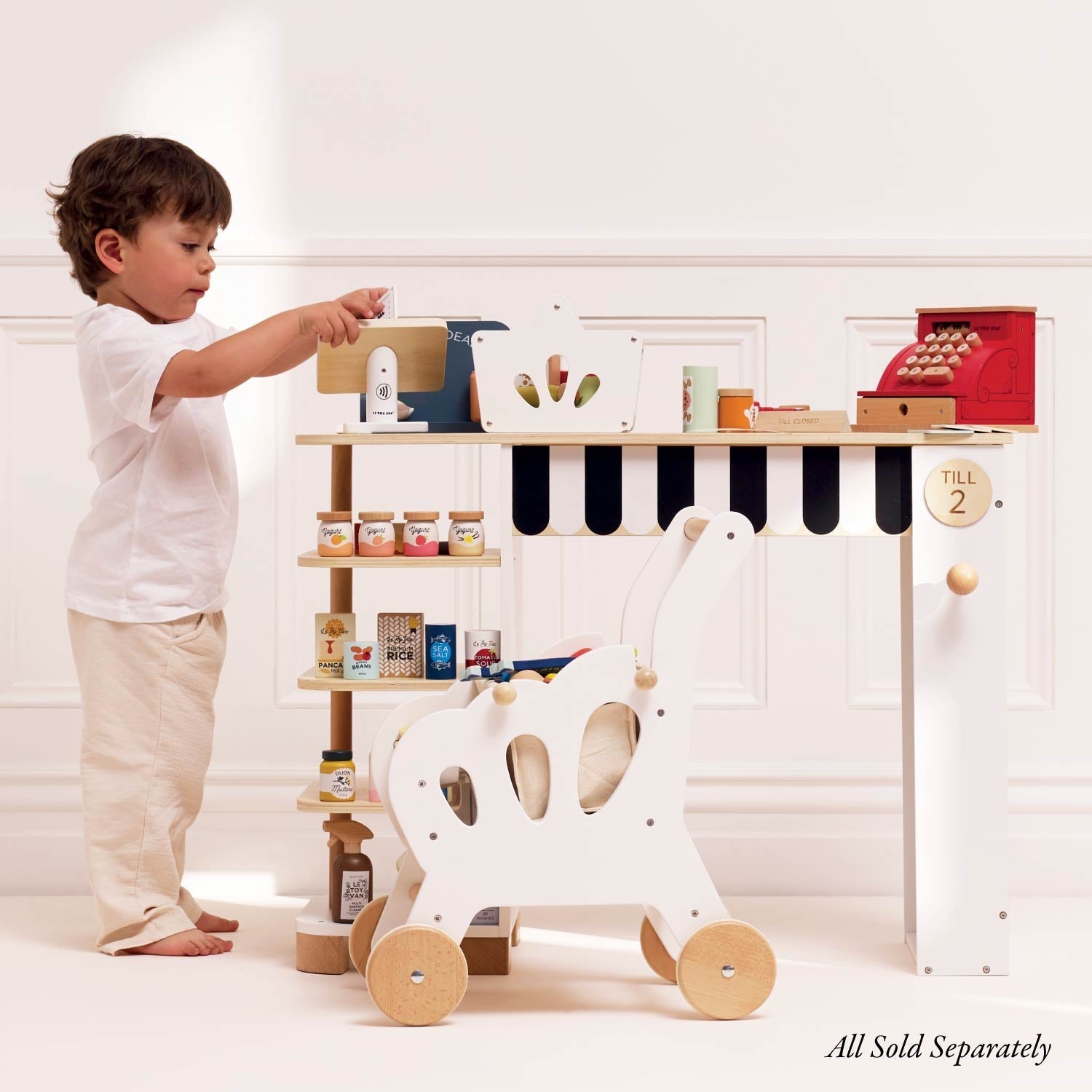 Child interacting with a toy store setup including a child's cart and various toys on a white background.