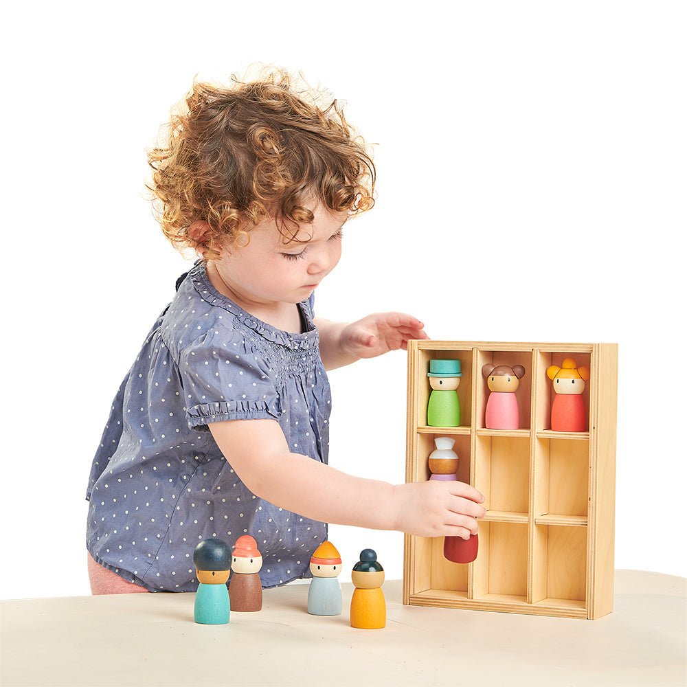 Child playing with a set of colorful wooden dolls in a box on a white background