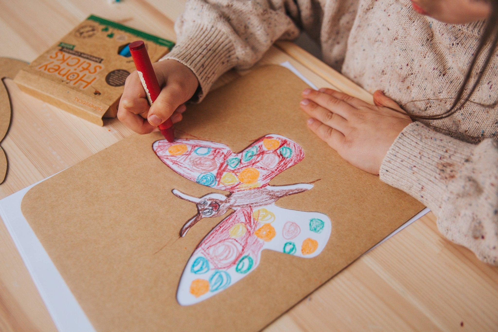 Child coloring a butterfly on brown paper with a red marker