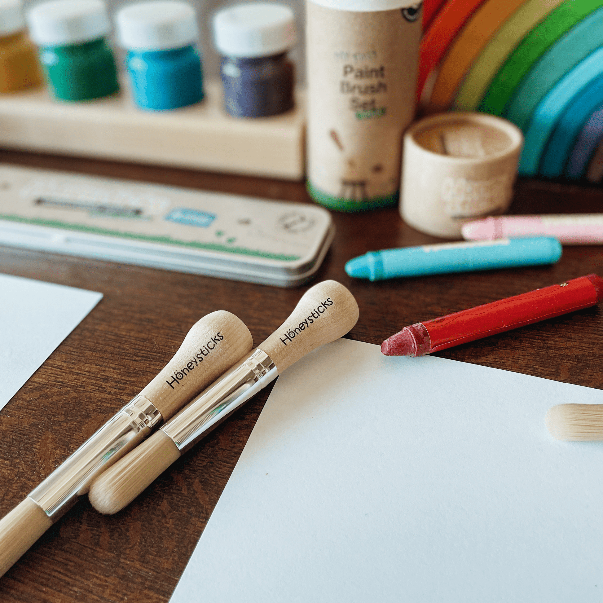 Paintbrushes with 'Honeysticks' branding on a wooden table with art supplies.