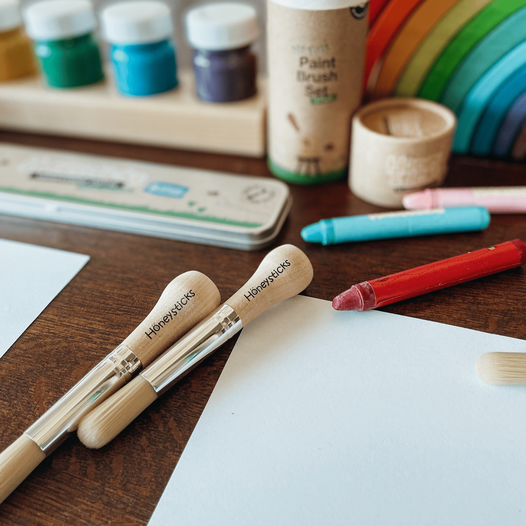 Paintbrushes with 'Honeysticks' branding on a wooden table with art supplies.