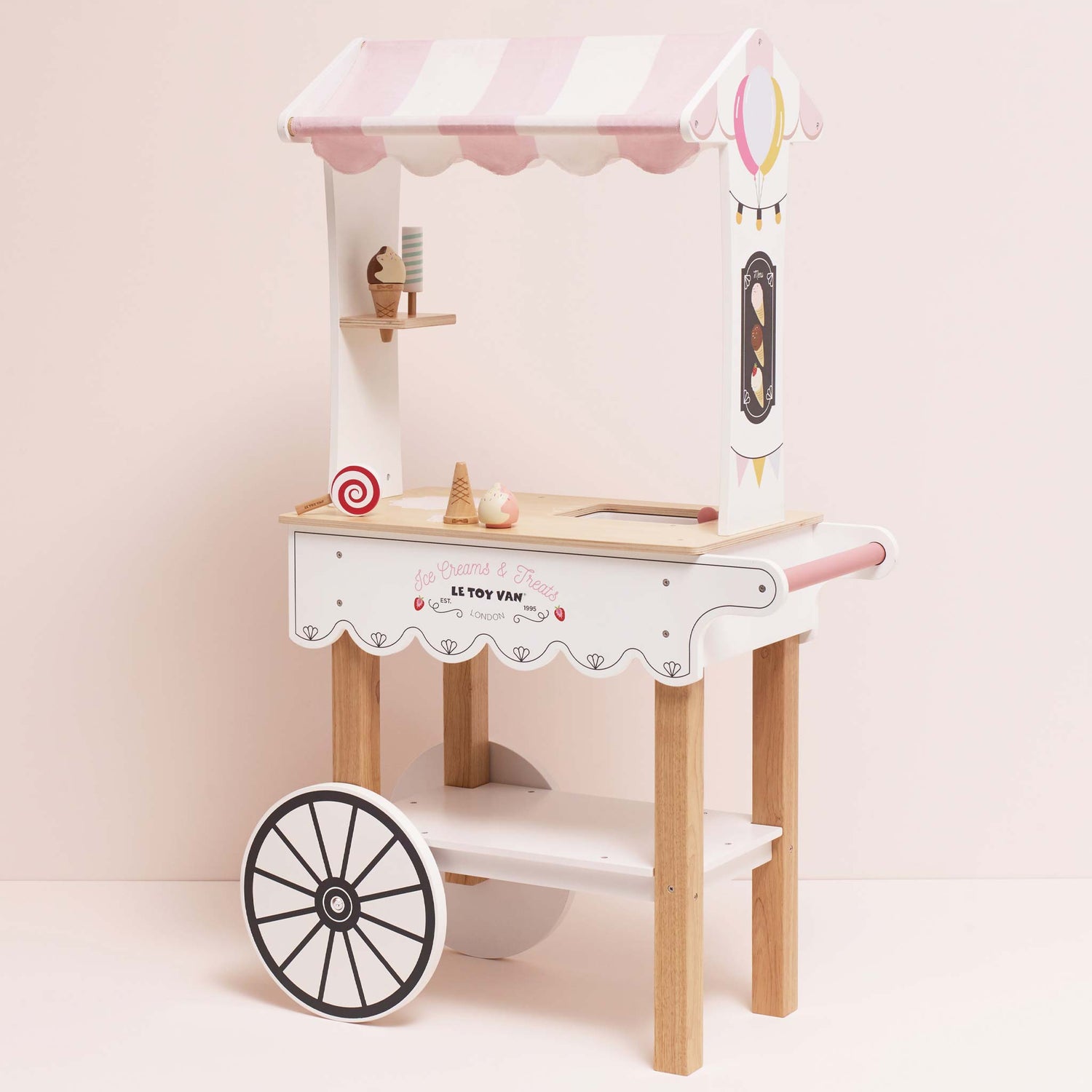 Children's toy ice cream cart with pink roof and wooden base on a light pink background