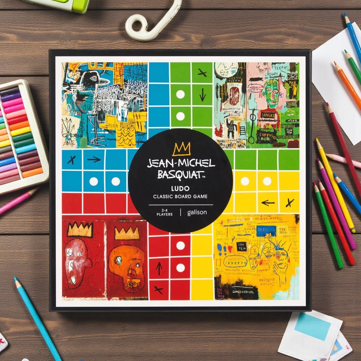 Jean-Michel Basquiat Ludo board game box on a wooden surface with art supplies.