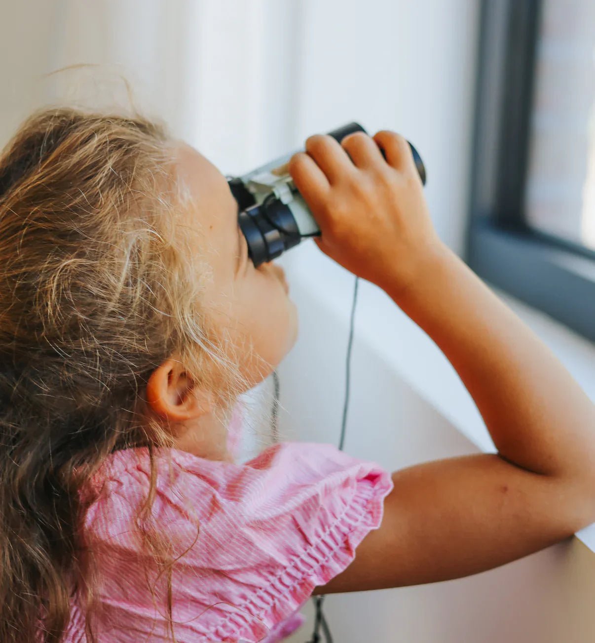Child looking through binoculars by a window