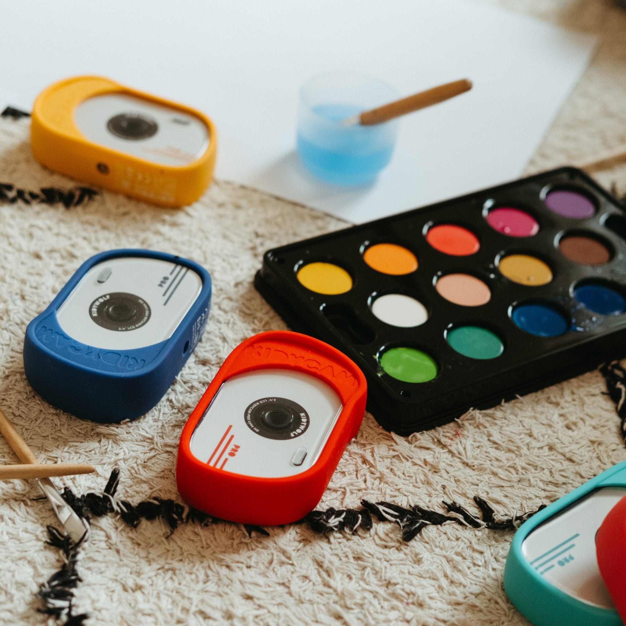 Colorful mini cameras and a watercolor palette on a textured surface