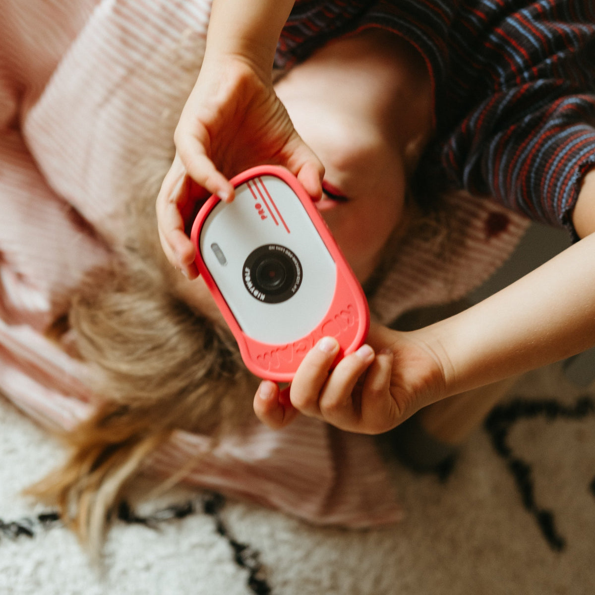 Child holding a red and white toy camera on a soft surface