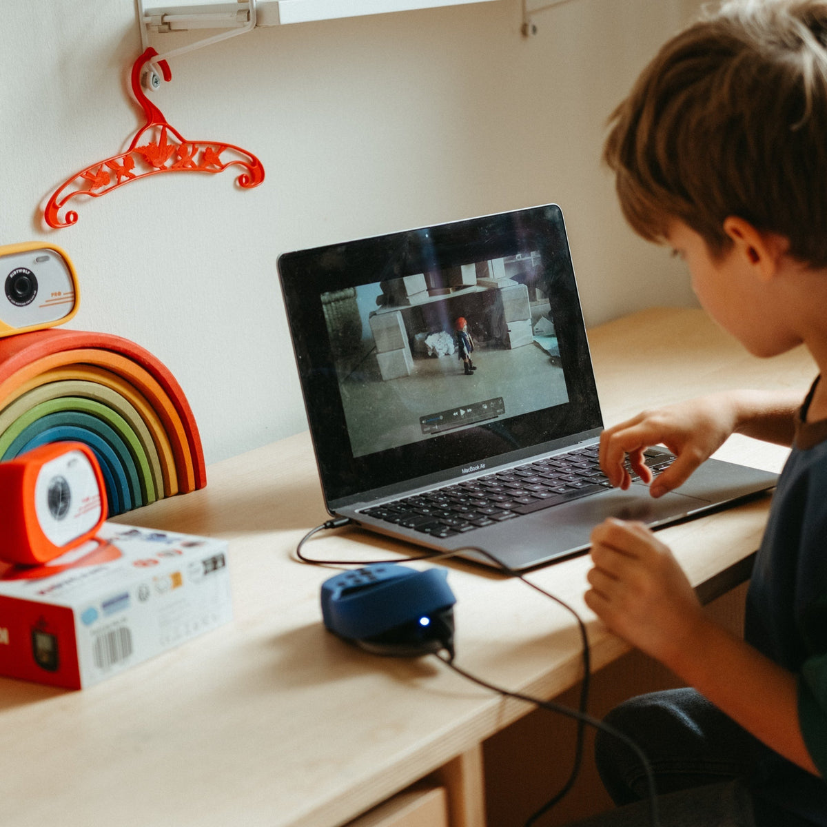 Child using a laptop on a desk with colorful objects around
