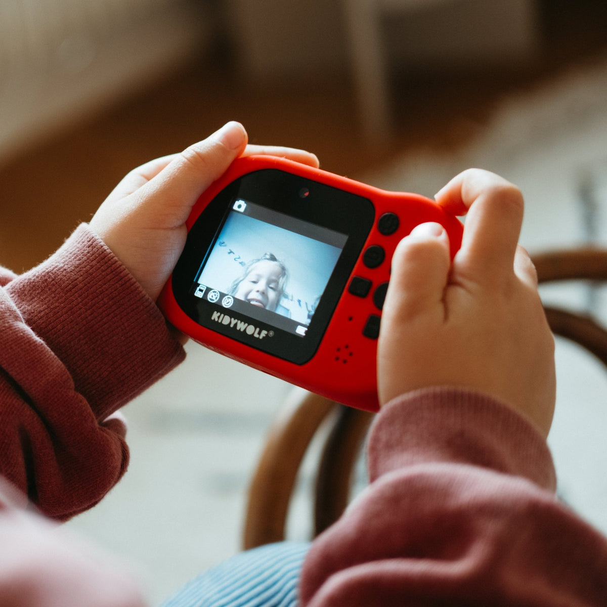 Red handheld gaming device with screen displaying graphics, held by two hands.