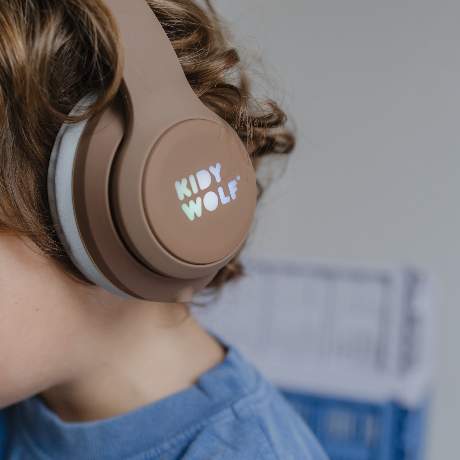 Person wearing brown headphones with 'KIDY WOLF' branding, holding a book.
