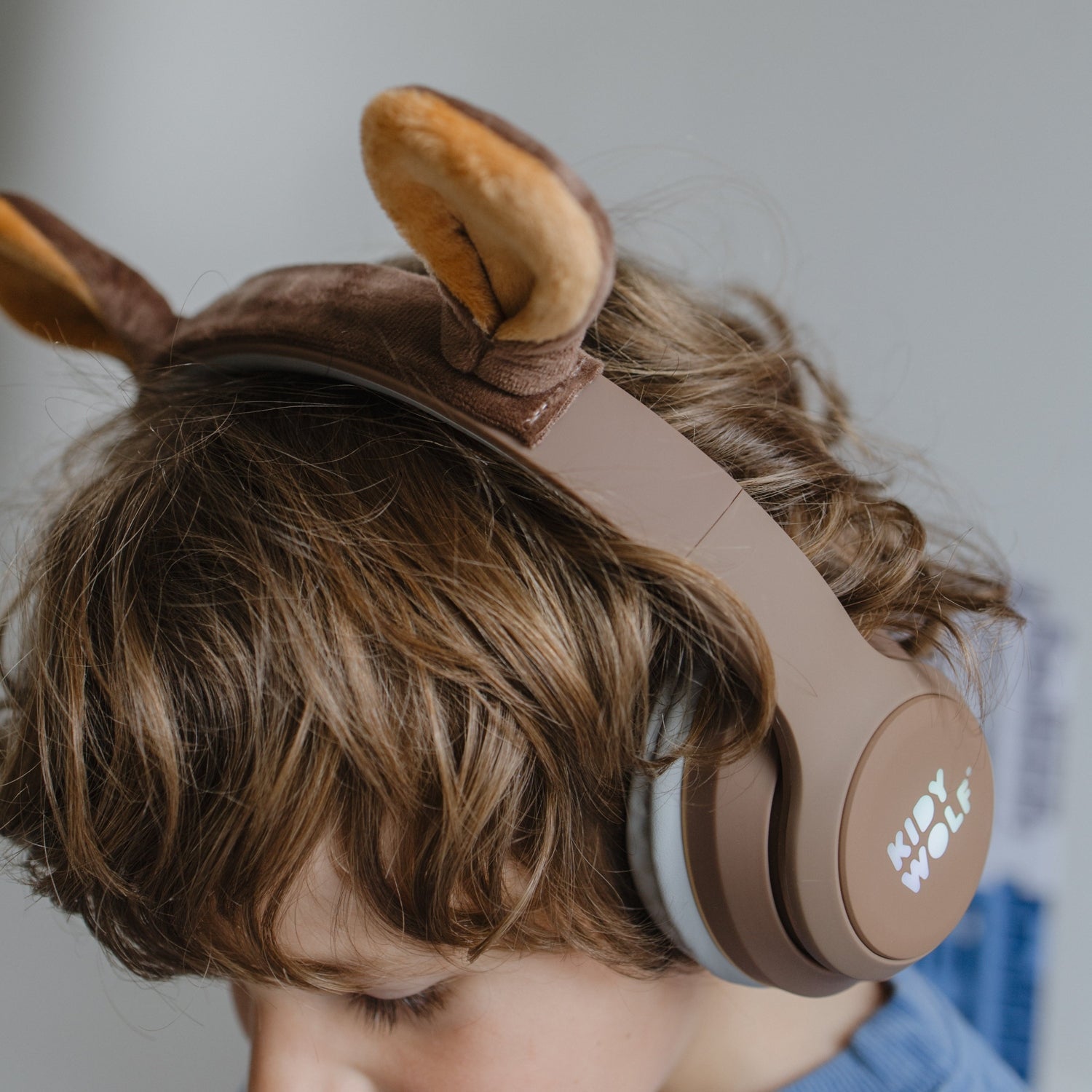 Child wearing brown headphones with animal ears, brand 'Kody Wolf' visible