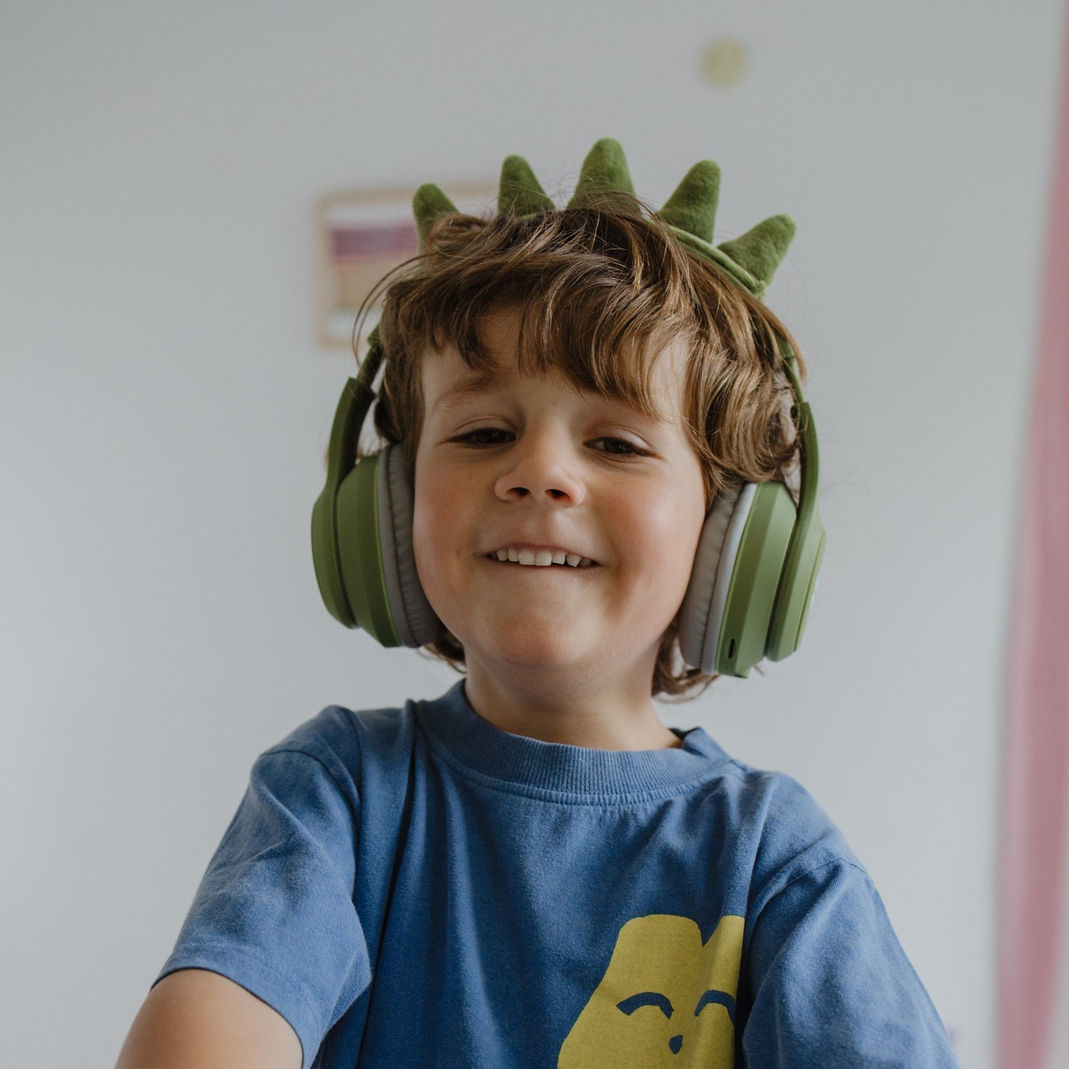 Child wearing green dinosaur headphones and a blue shirt with a yellow logo.