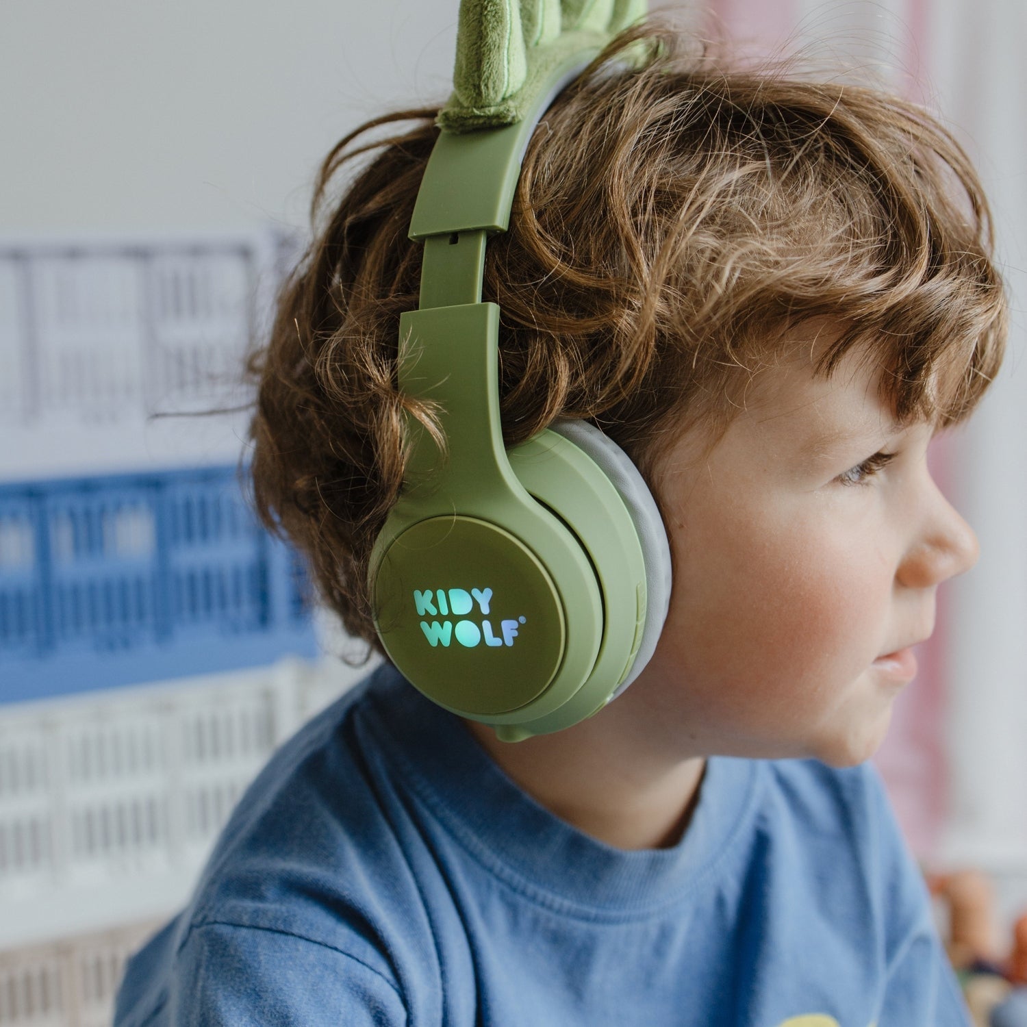 Child wearing green headphones with 'KIDLY WOLF' branding, sitting indoors.