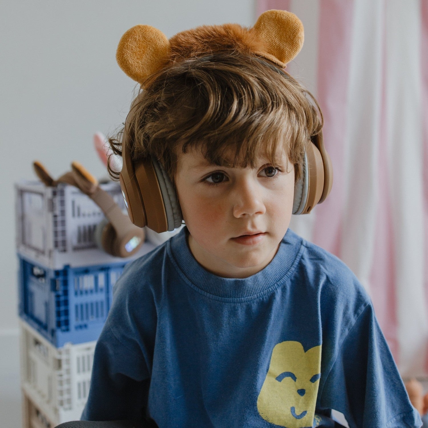 Child wearing large headphones with bear ears in a room with toys and a pink curtain.