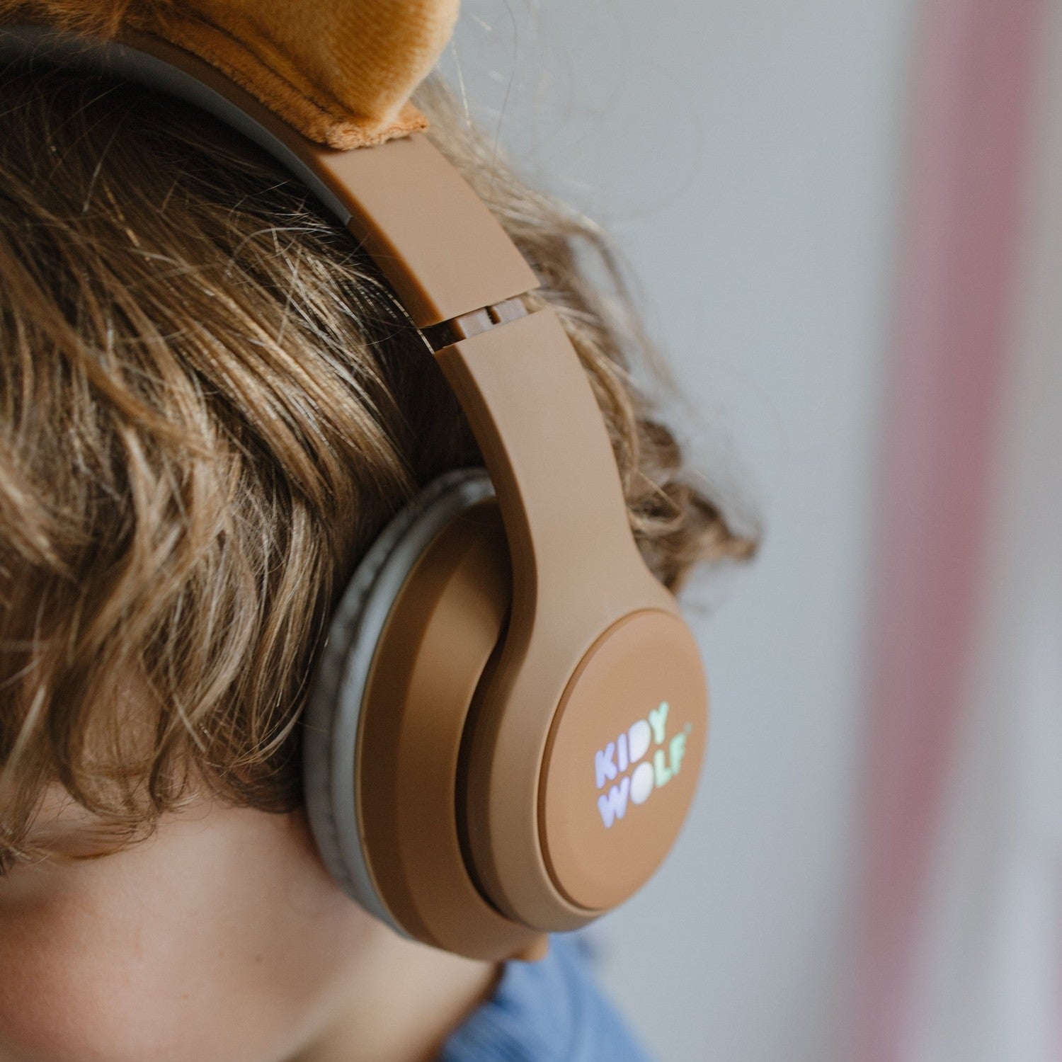 Person wearing brown headphones with 'K moy Wolf' branding against a blurred background