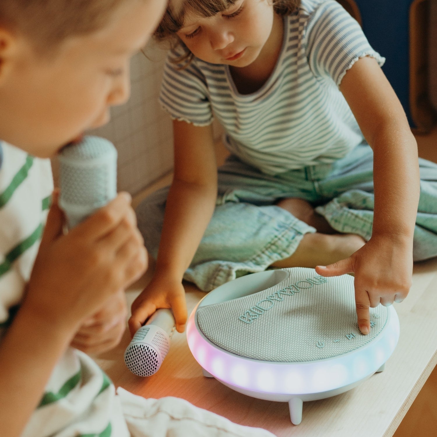 Two children playing with a toy device and microphones on a wooden floor.