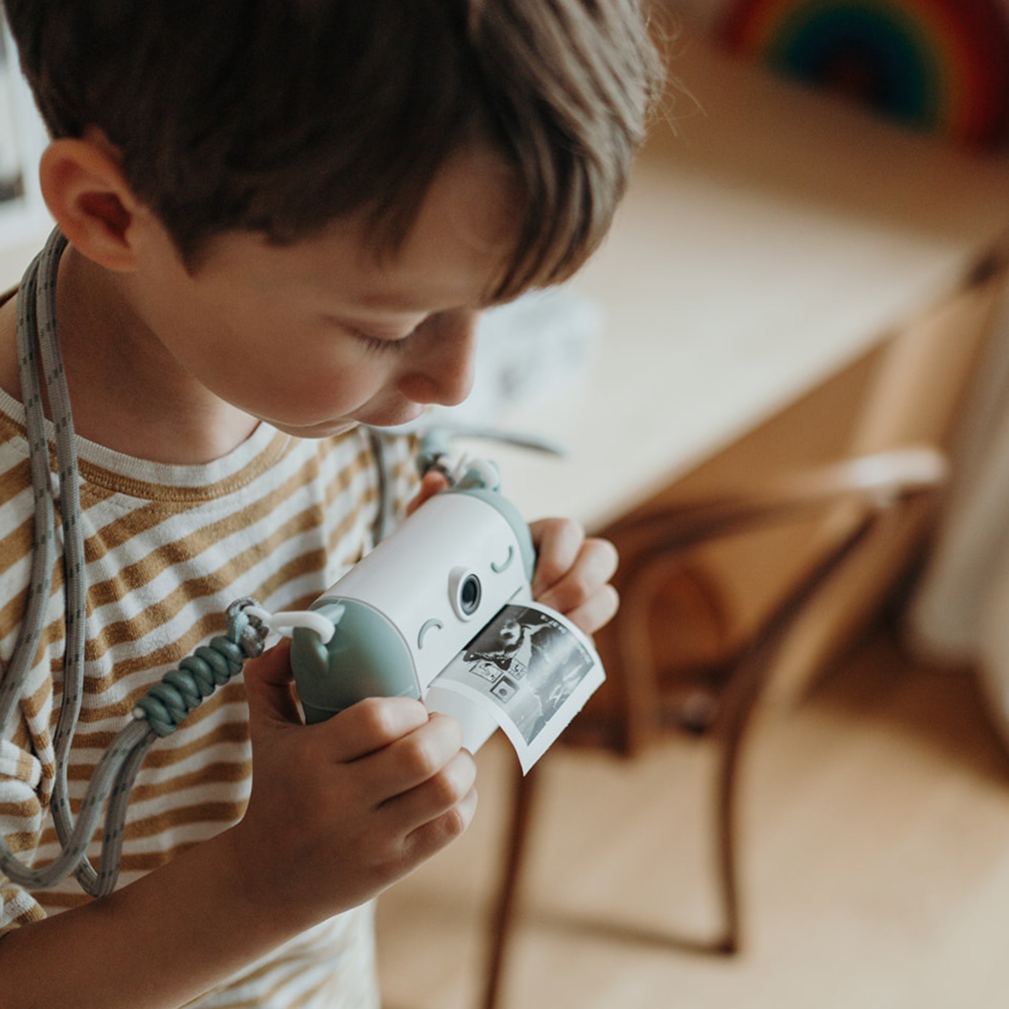 Child holding a toy camera with a photo printed on it, indoors.