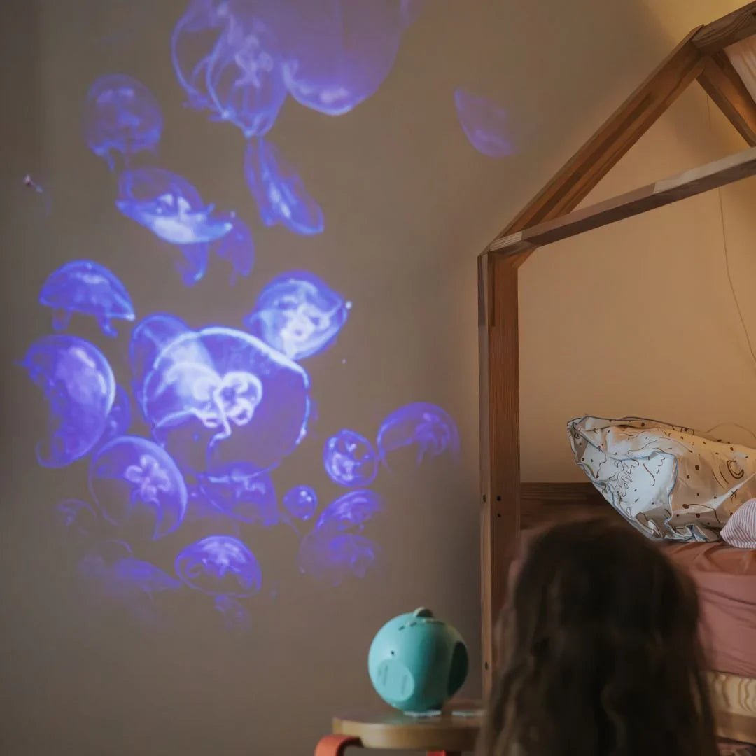 Children's room with jellyfish projections on the wall and a child sitting on a bed.
