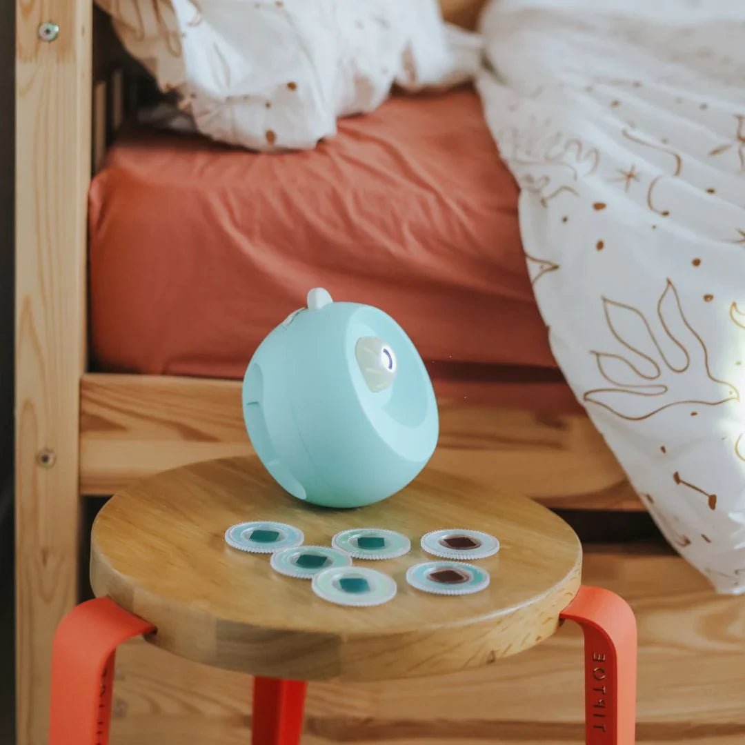 Small turquoise robot on a wooden stool with colorful buttons in a cozy room.