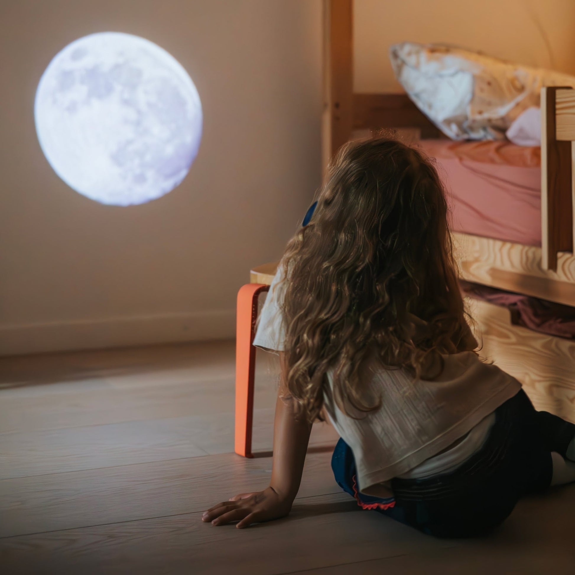 Child sitting on the floor looking at a projected moon in a bedroom.
