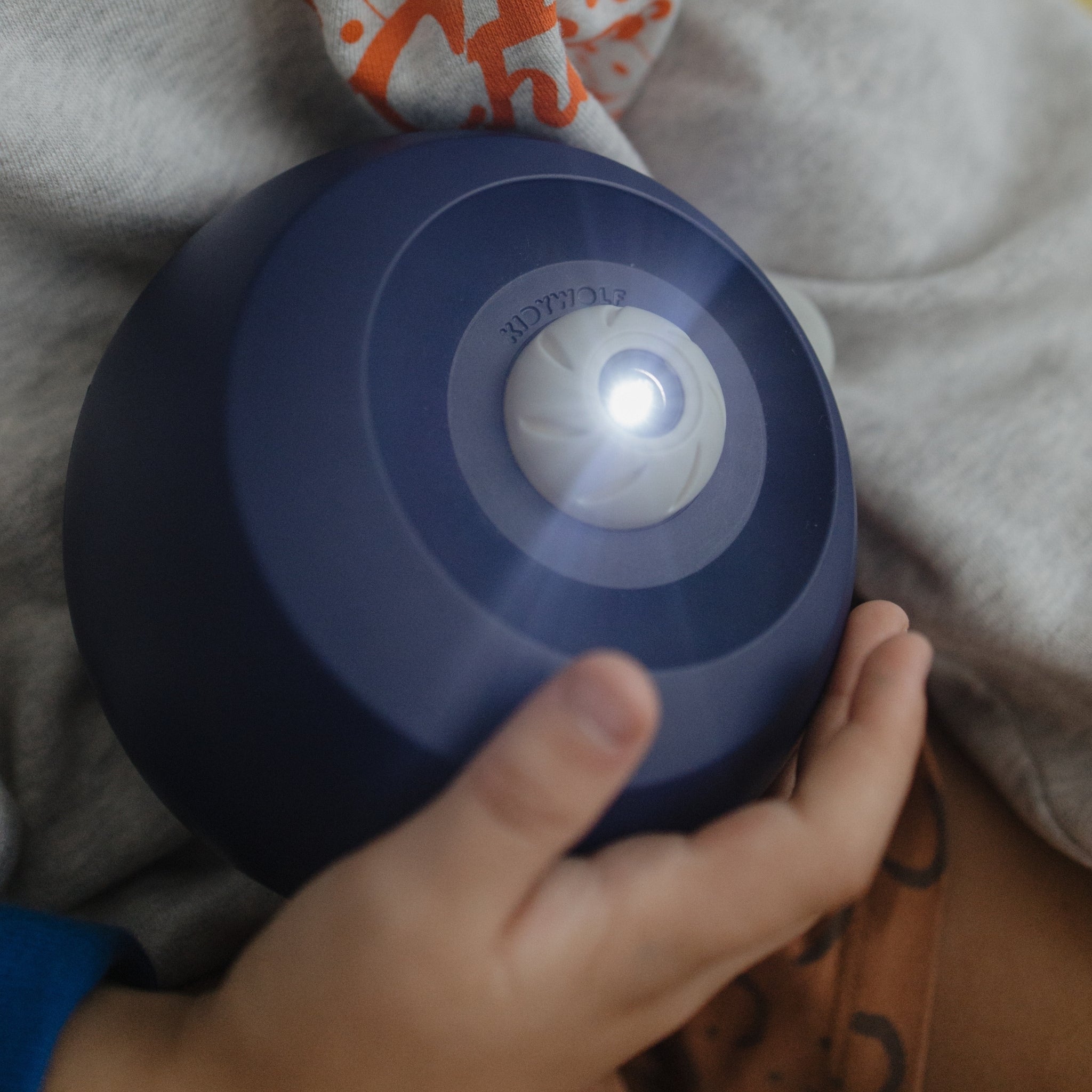 Hand holding a blue night light on a soft surface