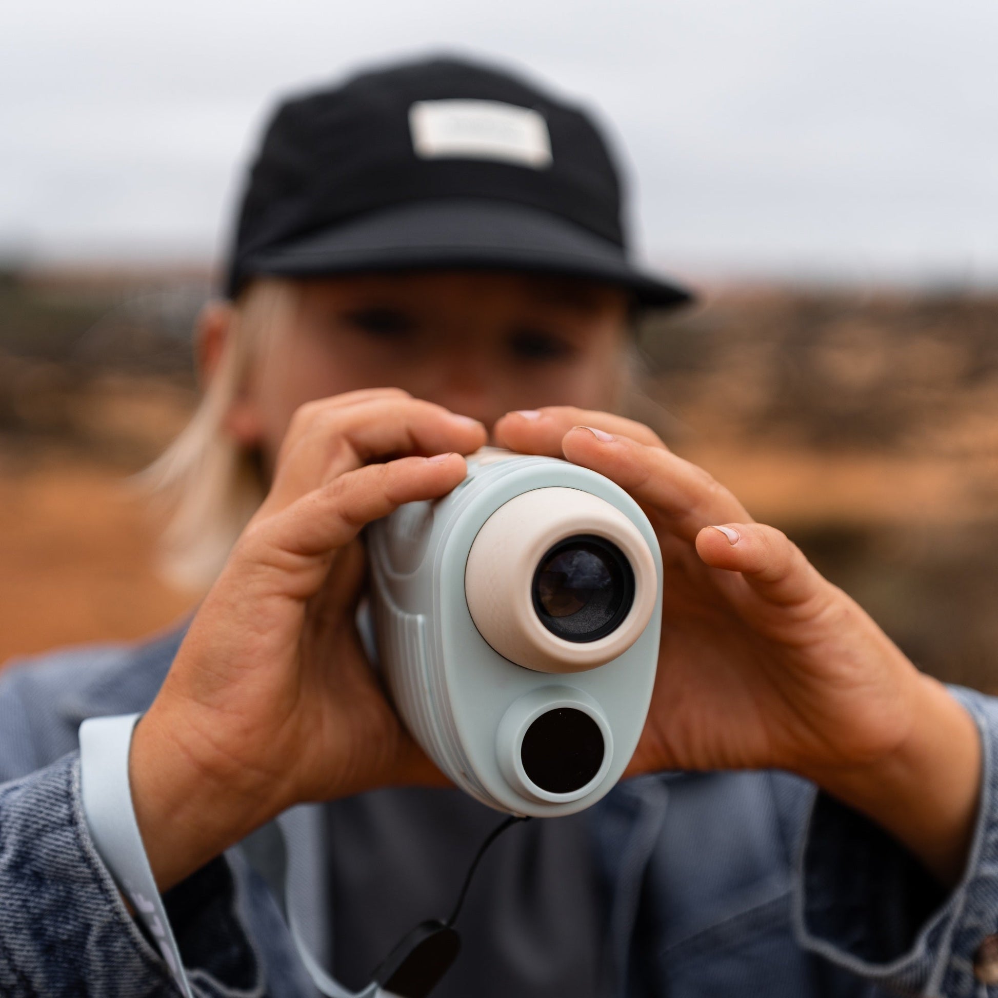 Person holding a white device with a lens, outdoors.