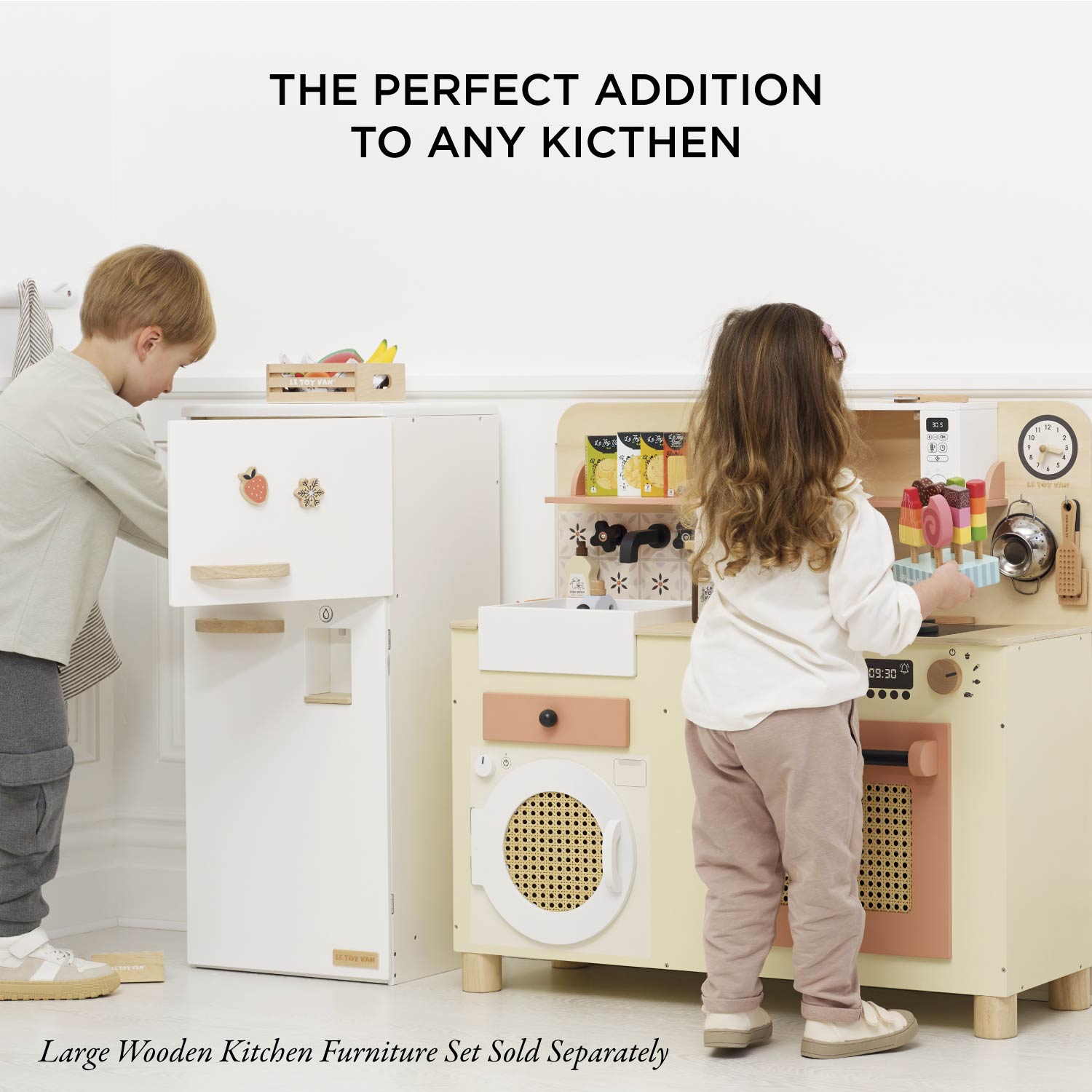 Children playing with a wooden kitchen set, with text 'The perfect addition to any kitchen' and 'Large Wooden Kitchen Furniture Set Sold Separately'.
