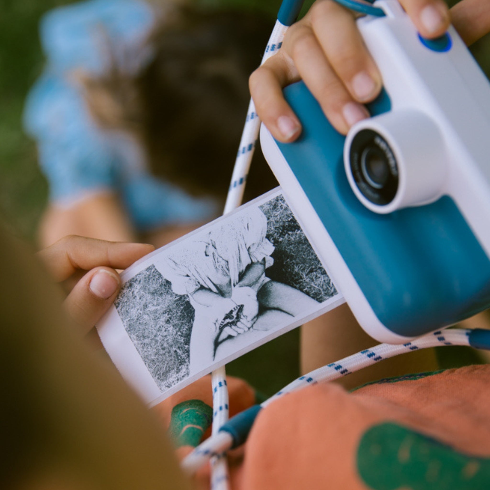 Person holding a blue and white camera with black and white photos attached, outdoors.