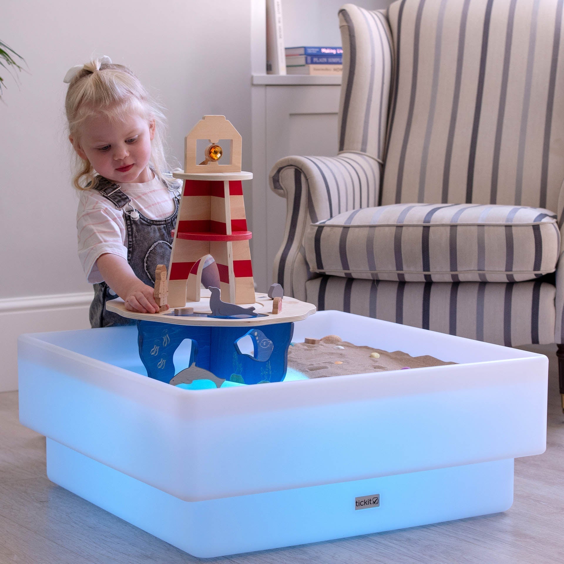 Child playing with a wooden lighthouse toy on a colorful LED play table.