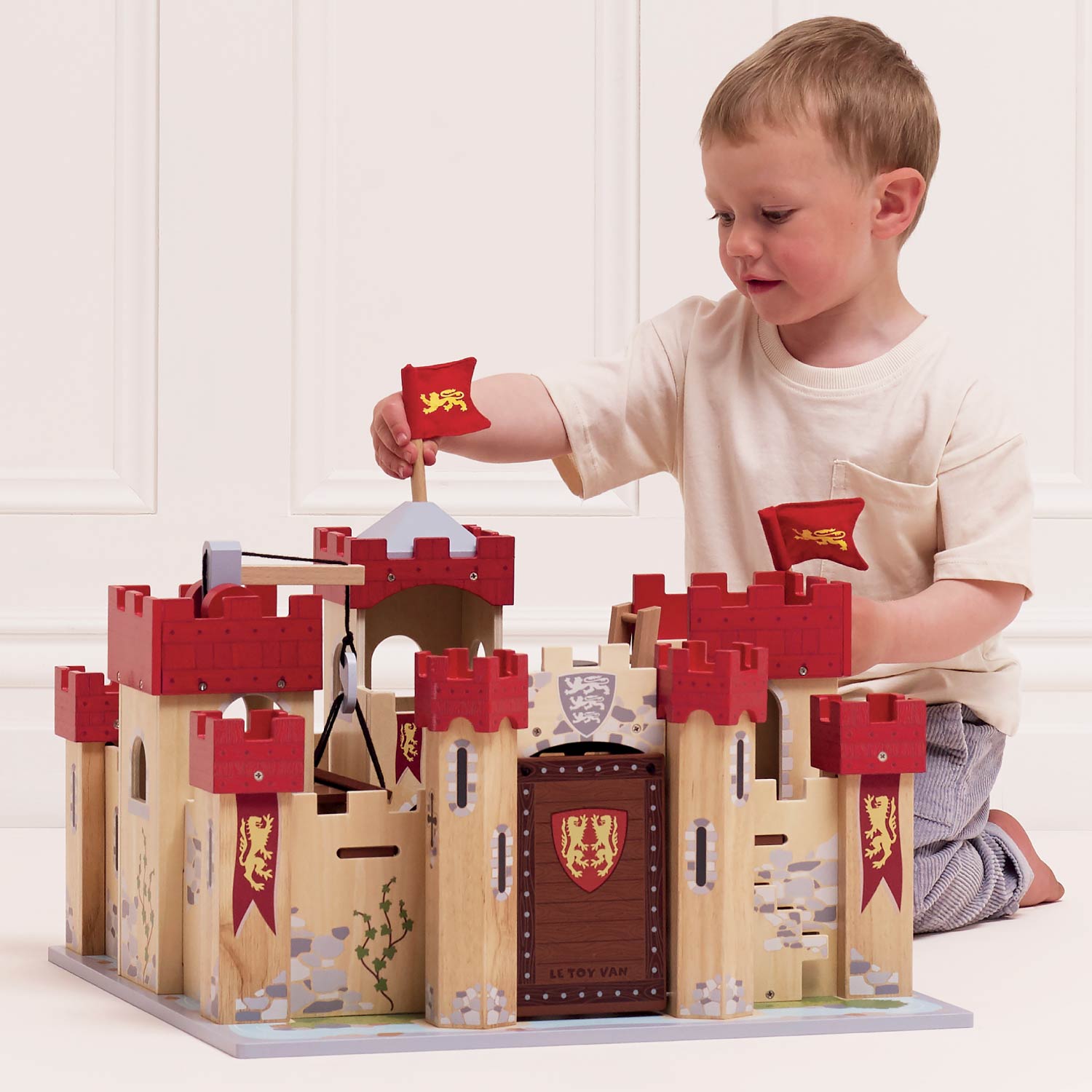 Child playing with a wooden toy castle set on a white background