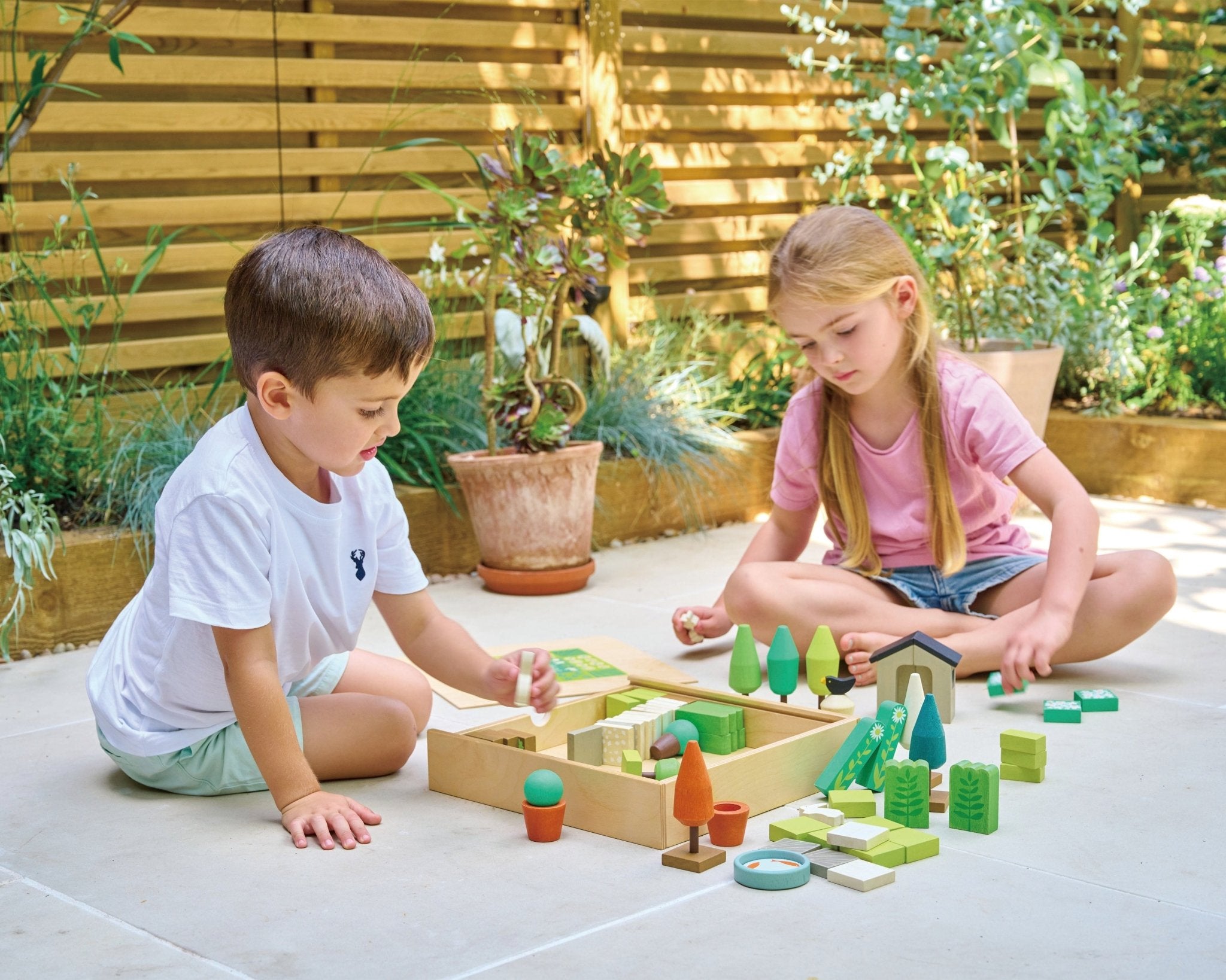 Two children playing with wooden toy blocks in a garden.