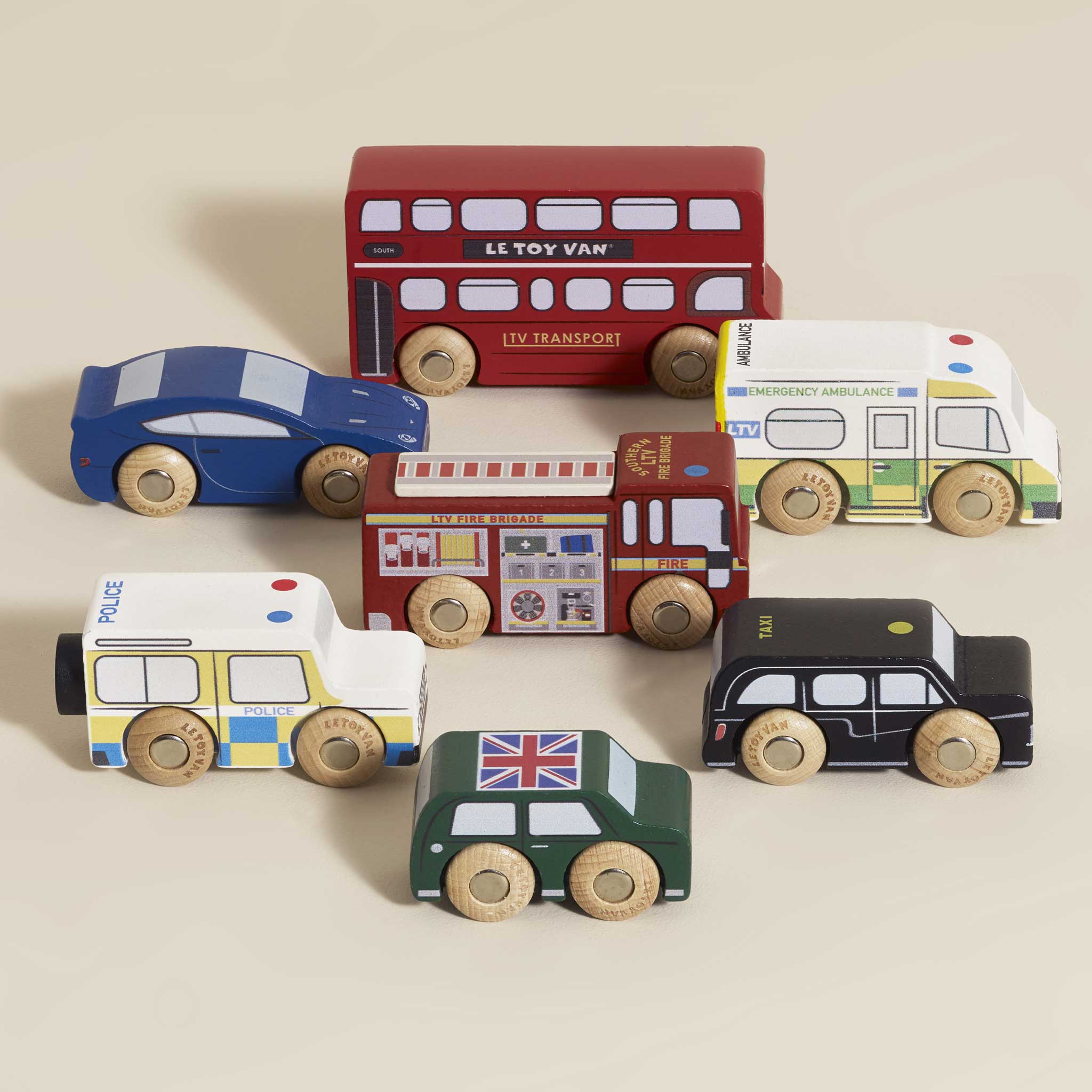 Set of wooden toy vehicles including a red bus, police car, fire truck, and others on a beige background.