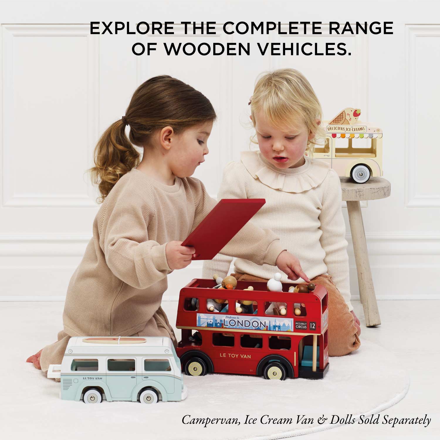 Two children playing with wooden toy vehicles on a white floor.