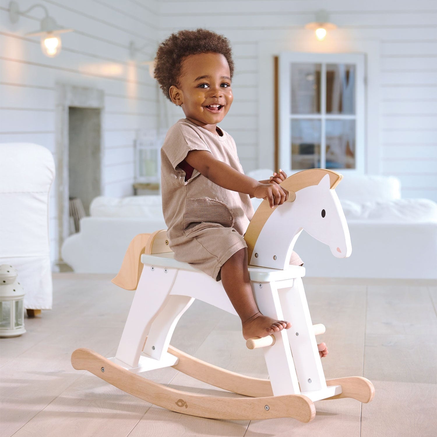 Child sitting on a wooden rocking horse in a bright room.