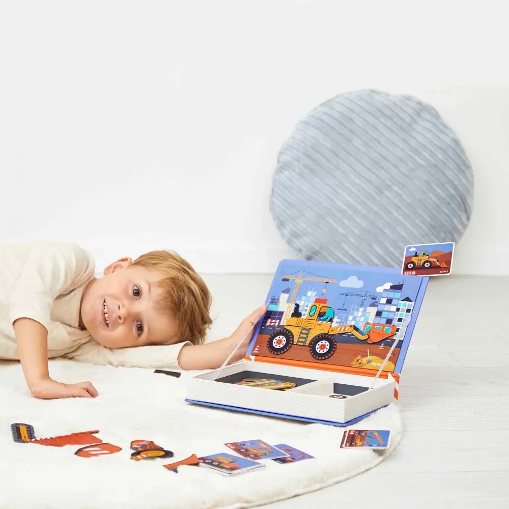 Child playing with a construction-themed book and toy on a white surface.