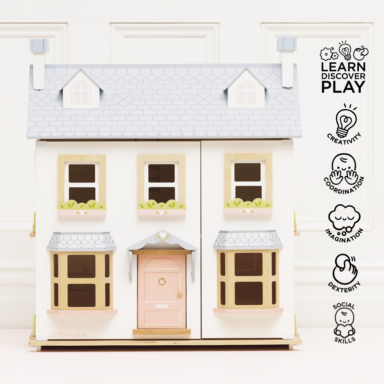 Model of a dollhouse with a pink door on a white background, featuring icons and text about learning, discovery, and play.