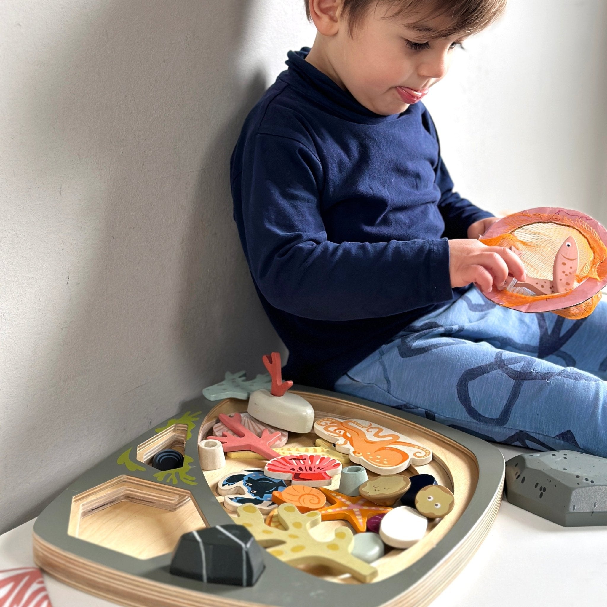 Child playing with a toy tray filled with colorful wooden animals on a white background