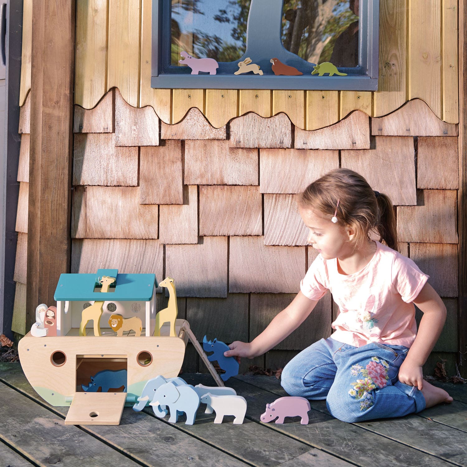 Child playing with a wooden toy Noah's Ark in front of a wooden playhouse.