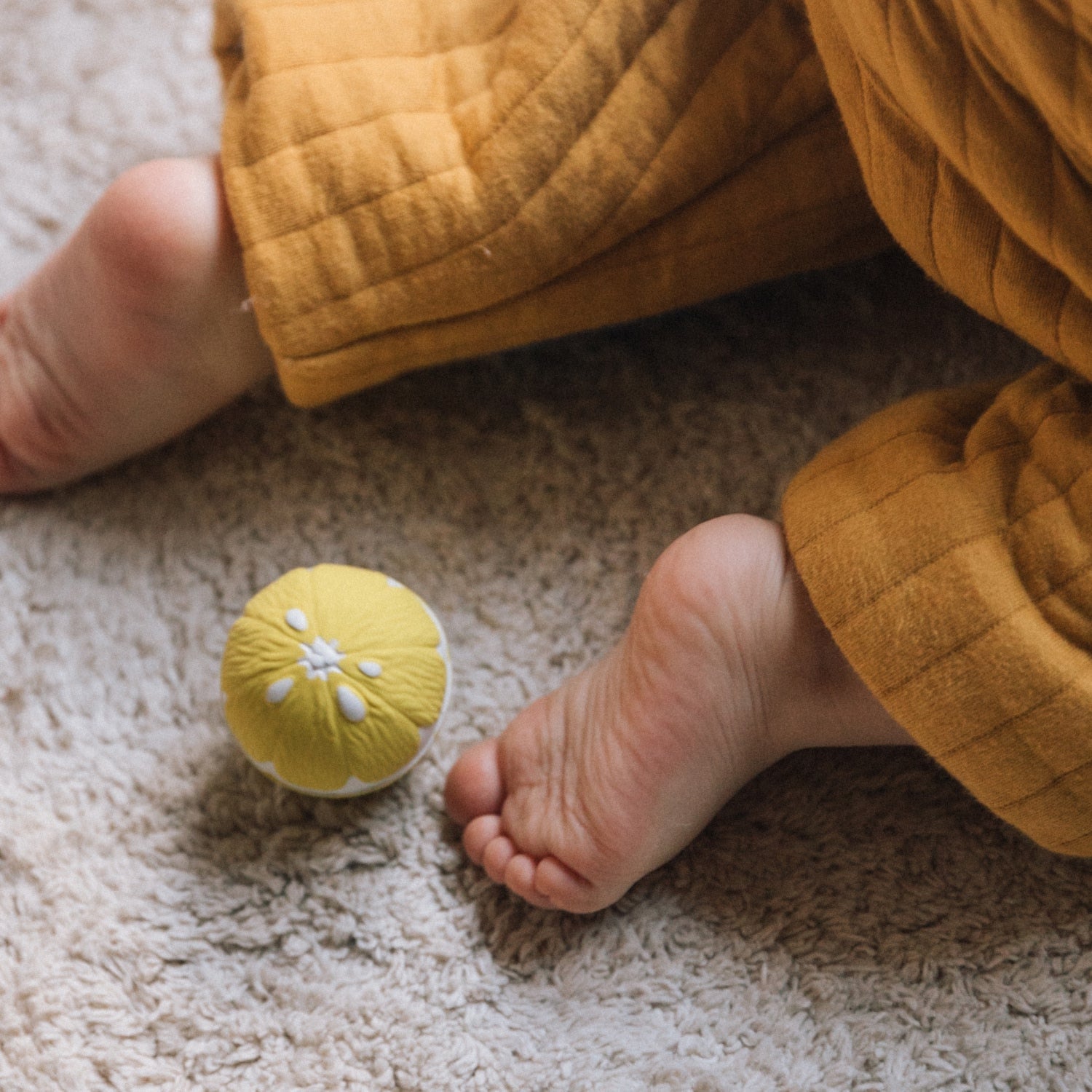 Baby's feet near a yellow ball on a carpeted floor