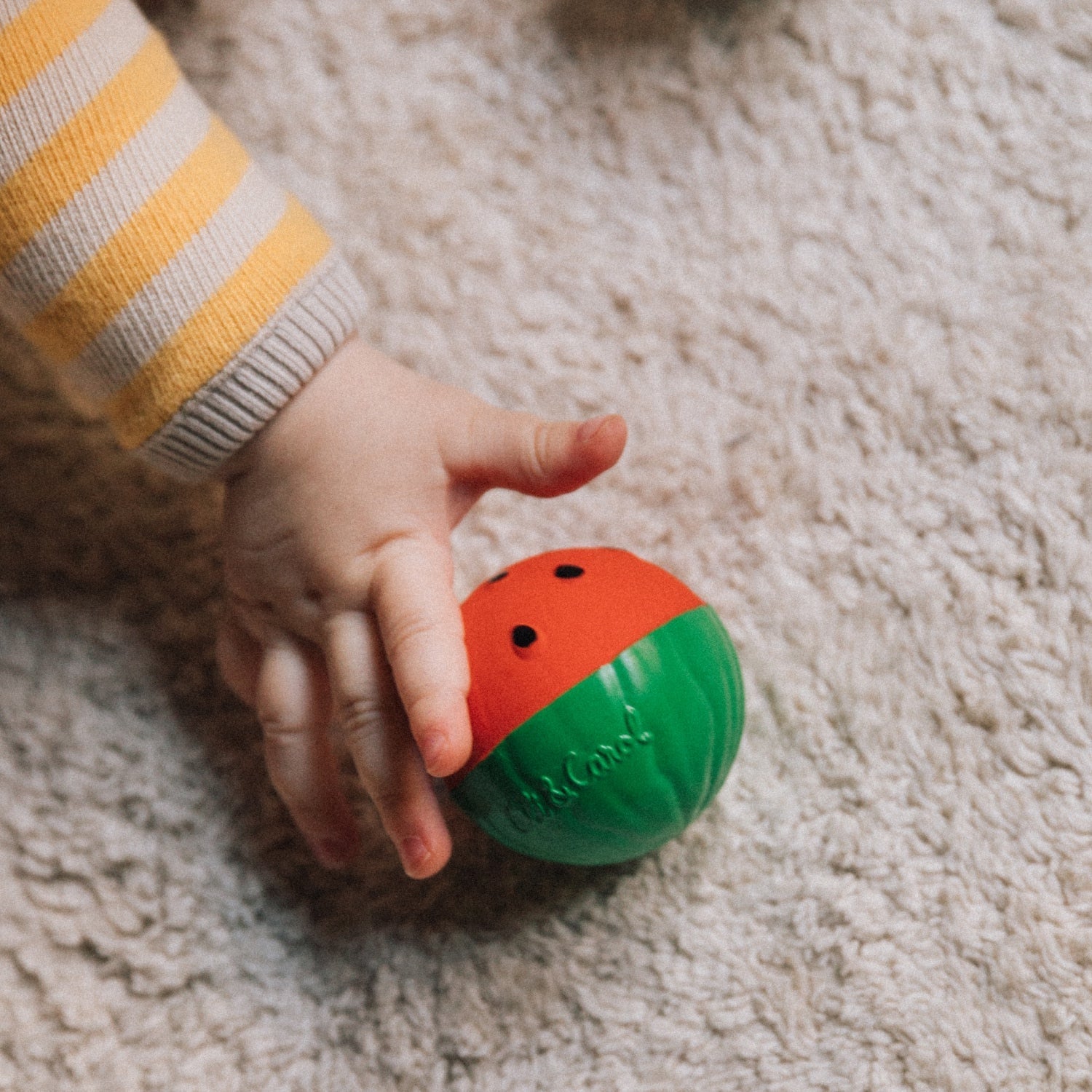 Child's hand holding a colorful ball on a carpeted floor