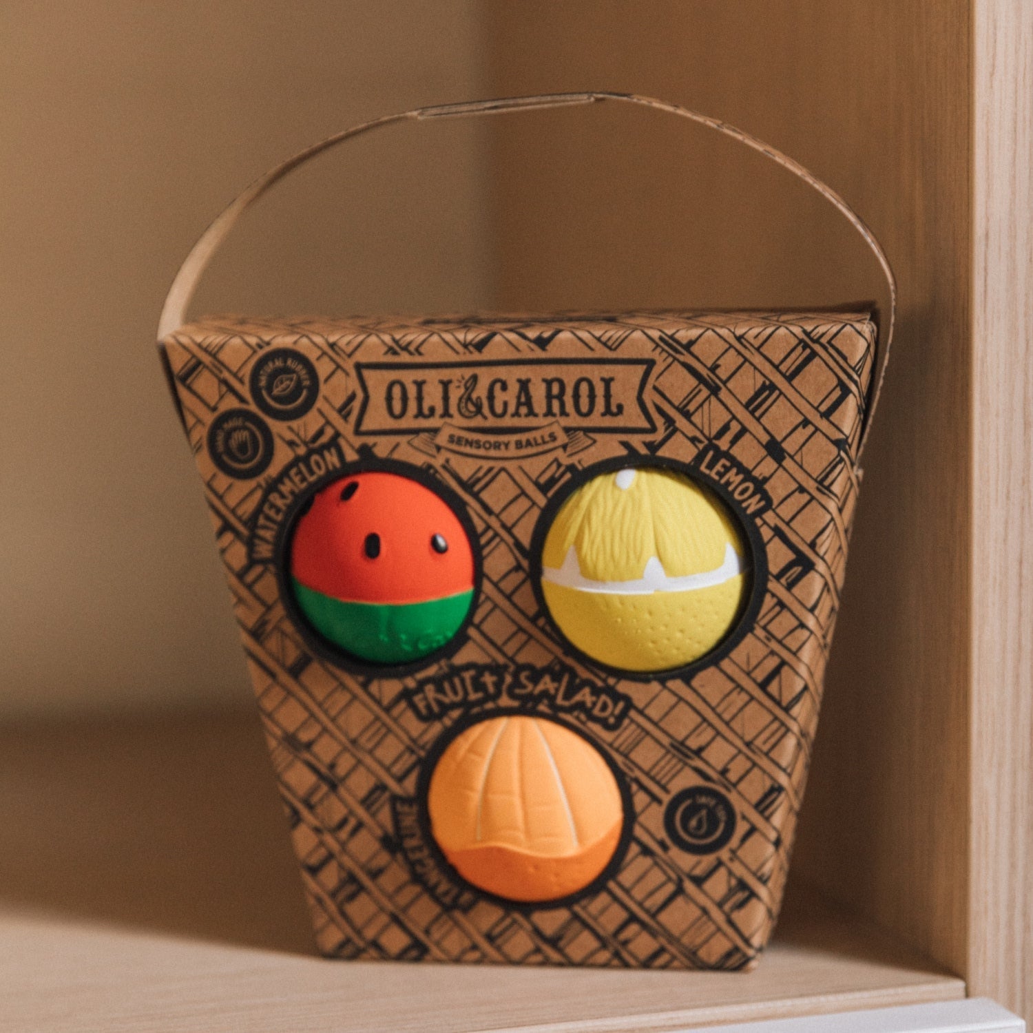 Basket with fruit-themed balls and 'Oli & Carol' branding on a wooden surface.