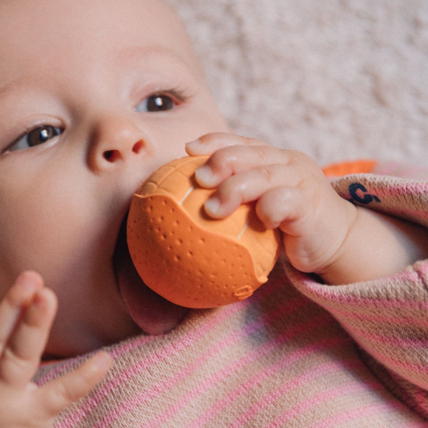 Baby holding an orange teething ball against a soft background