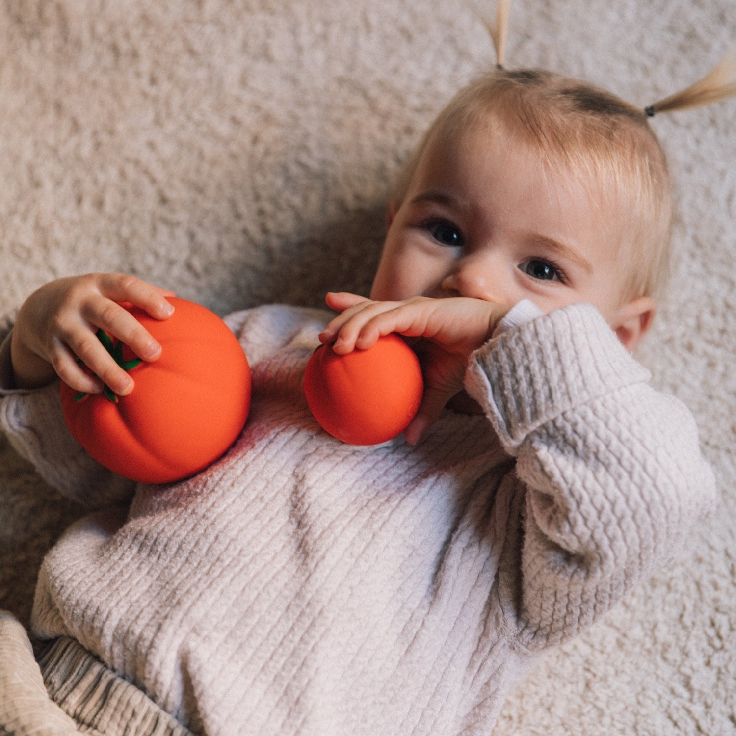 Child holding two orange toys against a neutral background