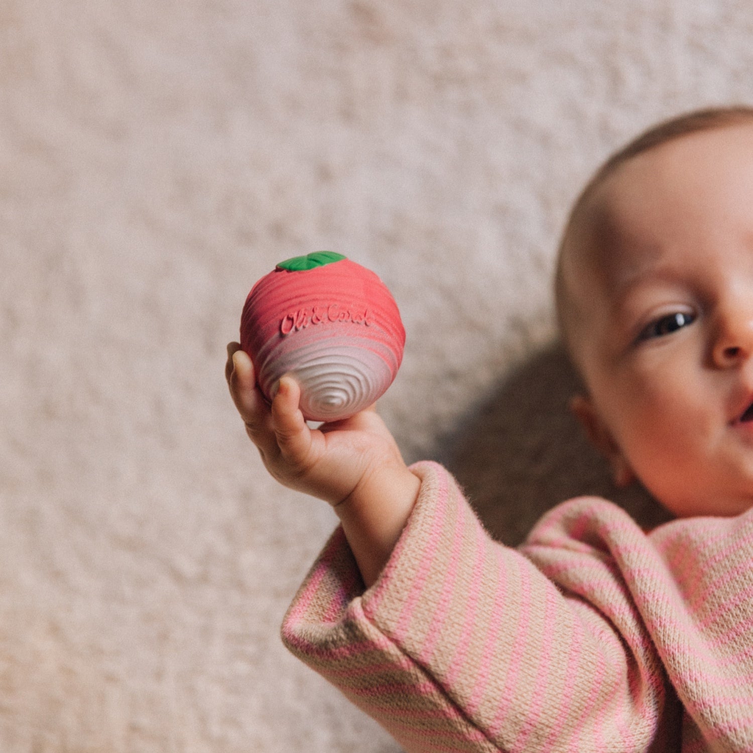 Baby holding a red teething ball with a neutral background